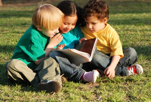Skupina dětí s knihou na trávě v parku — Stock fotografie