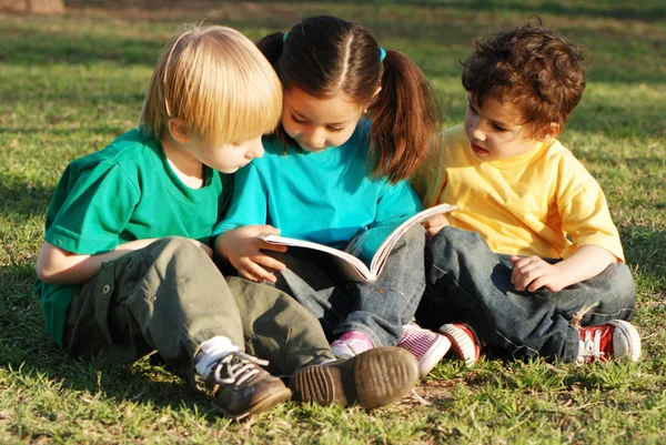 Groep van kinderen met het boek op een gras in park — Stockfoto