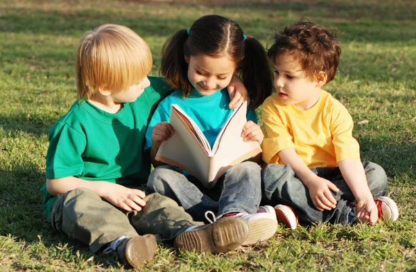 Grupa dzieci z książki na trawie w parku — Zdjęcie stockowe