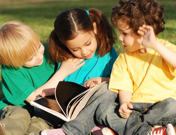 Group of children with the book on a grass in park — Stock Photo, Image