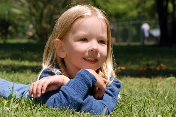 Das kleine Mädchen liegt auf einer Wiese im Park — Stockfoto