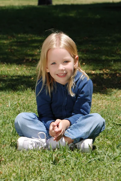Девочка, сидящая на траве в парке — стоковое фото