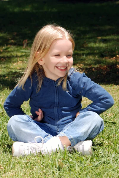 Parkta çim üzerinde oturan küçük kız — Stok fotoğraf