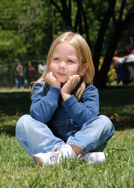 Das kleine Mädchen, das auf einem Gras im Park sitzt — Stockfoto