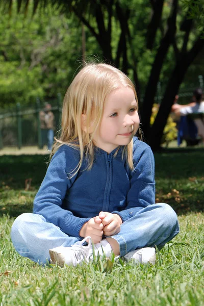 Parkta çim üzerinde oturan küçük kız — Stok fotoğraf