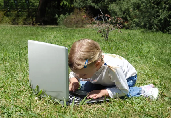 Маленькая девочка с ноутбуком на поляне в парке — стоковое фото