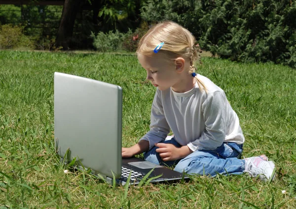 A menina com o computador portátil em uma clareira no parque — Fotografia de Stock