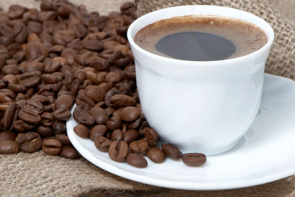 Detail šálku kávy nad tmavě pražená kávová zrna — Stock fotografie