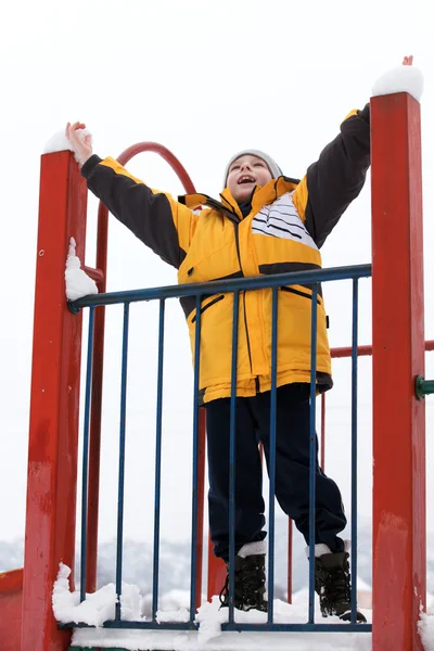 O rapaz com as mãos levantadas num parque infantil — Fotografia de Stock