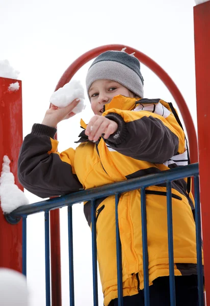 Il ragazzo che gioca palle di neve su un parco giochi da bambini — Foto Stock