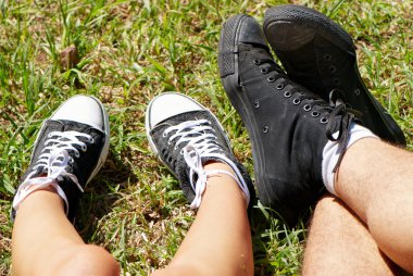 Feet of teenagers and gym shoes on a green grass of a lawn in p clipart