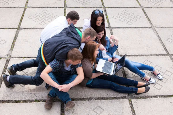 组的男学生和女学生坐在一起在大街上的一台笔记本电脑 — 图库照片