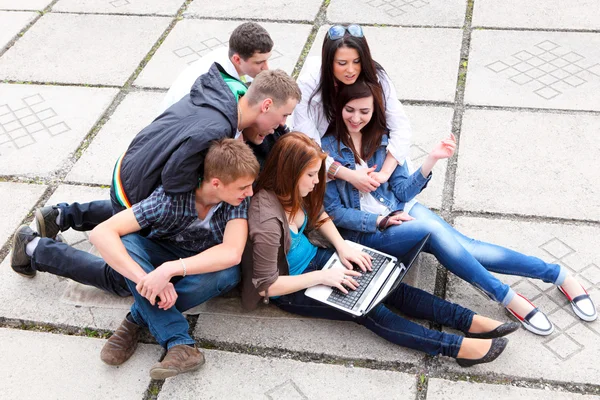组的男学生和女学生坐在一起在大街上的一台笔记本电脑 — 图库照片