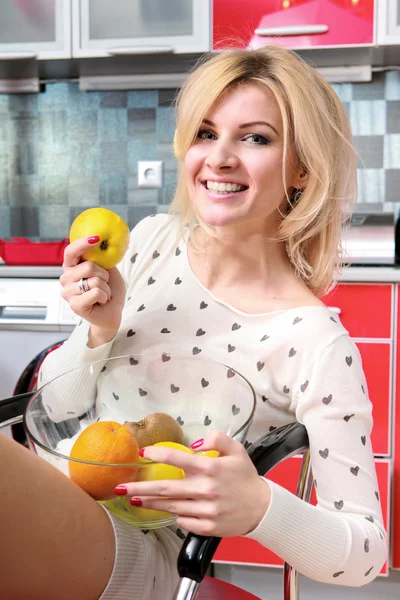 Αρκετά χαμογελαστό νεαρή γυναίκα κάθεται στην κουζίνα με φρούτα — Φωτογραφία Αρχείου