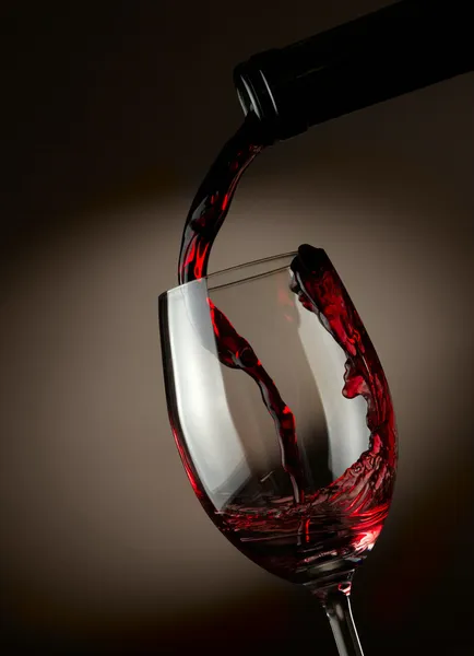 Красное вино льется в стакан на темном фоне — стоковое фото