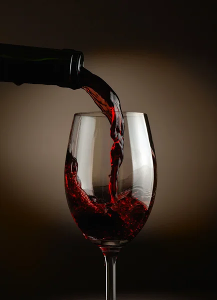 Rødvin hældes i glas over mørk baggrund - Stock-foto