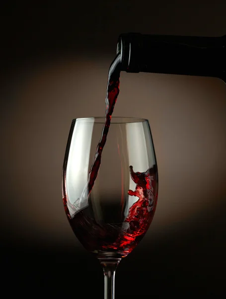 Red wine pouring into glass over dark background — Stock Photo, Image