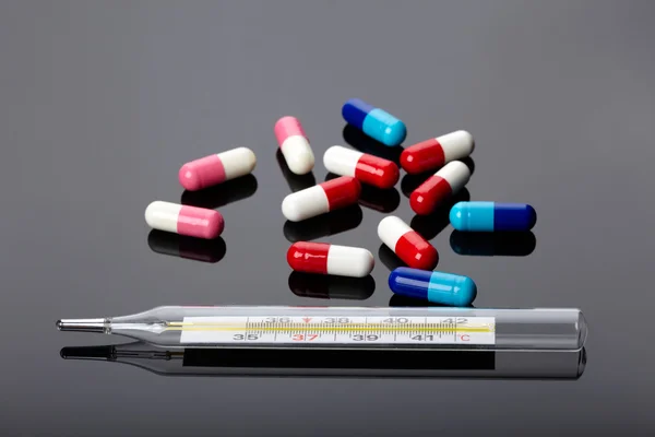 Pills and thermometer over dark background — Stock Photo, Image