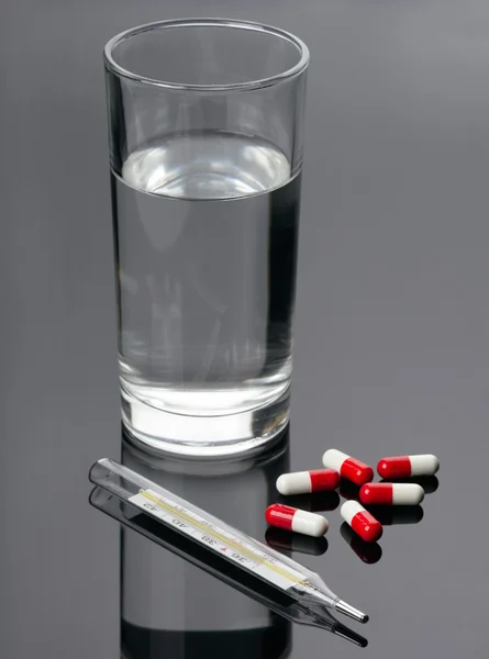 Stock image Pills, thermometer and glass of water over black background