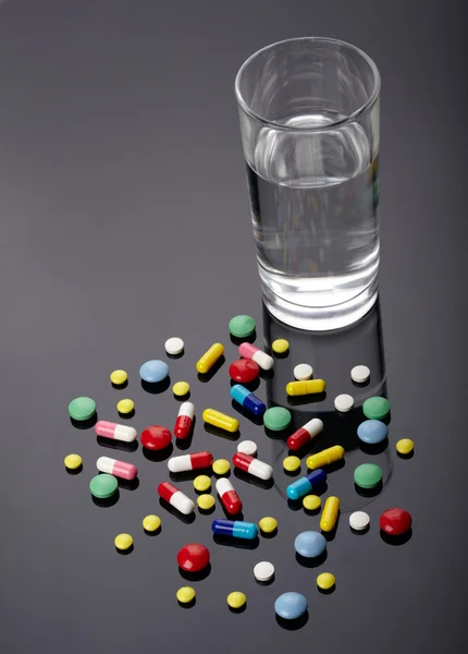 Pills and glass of water over dark background — Stock Photo, Image