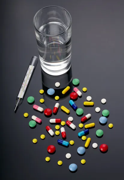 Pills, thermometer and glass of water over dark background — Stock Photo, Image