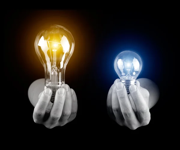 Mãos segurando duas lâmpadas isoladas em preto — Fotografia de Stock
