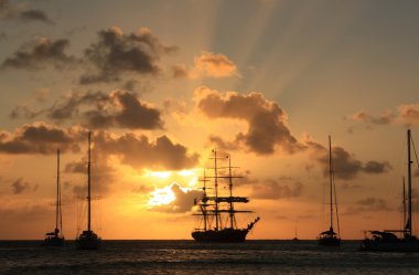 Caribbean sunset and silhouett of the ship and sailboats clipart