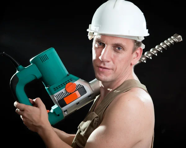 O construtor em um capacete protetor mantém o puncher-martelo profissional com uma furadeira do grande diâmetro — Fotografia de Stock