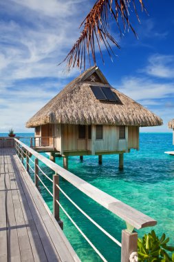 The wooden bridge to a hut over water at the ocean clipart