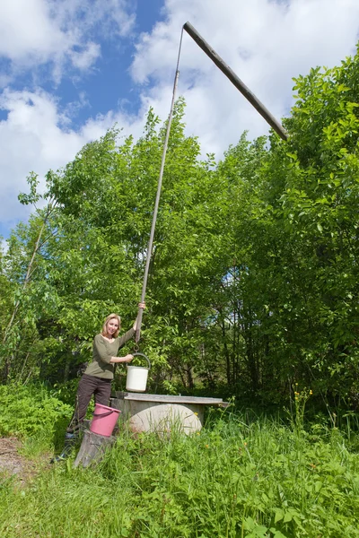 井戸の若い女性はバケツに水を注ぐ — ストック写真