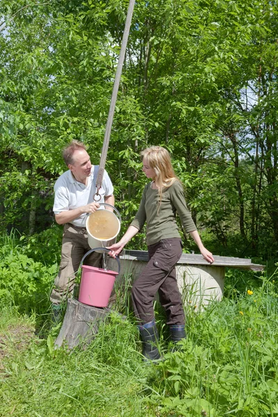 Young happy pair at a well, pours water in a bucket — Stock Photo, Image