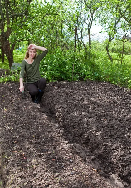 Den unga kvinnan soffan en trädgård-säng med första skott av potatis på en sommarstuga — Stockfoto