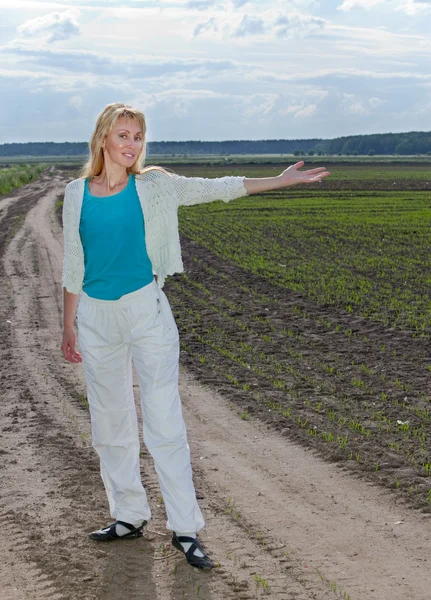 La joven en el camino rural muestra una mano en el campo con los primeros brotes —  Fotos de Stock