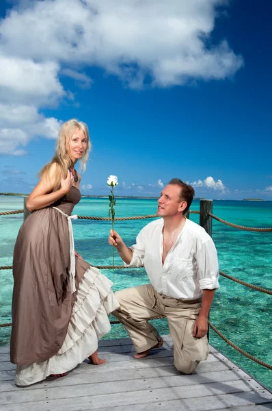 El hombre da una rosa a la mujer sobre el fondo de mar turquesa . — Foto de Stock