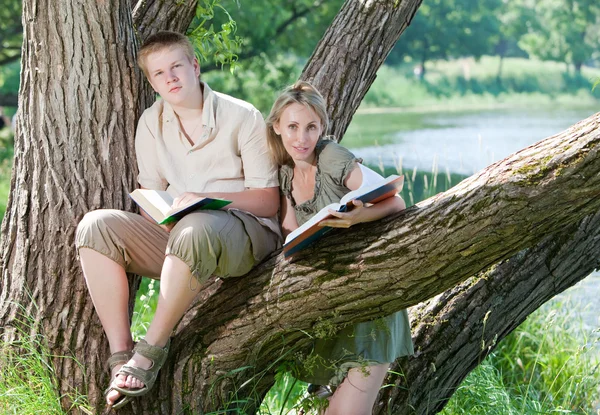 Chico joven y la chica con libros de texto en la orilla del lago — Foto de Stock