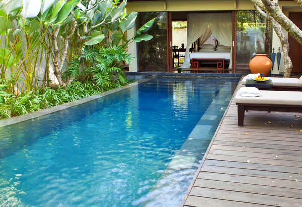 Bed under bed curtains and chaise lounges near pool