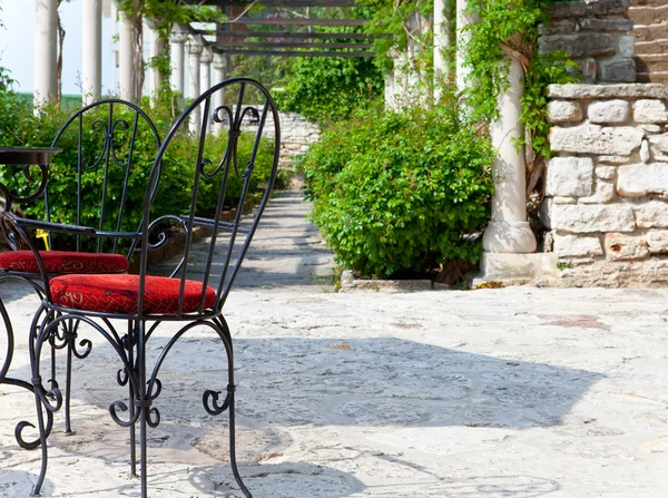 Shod chairs on the stone avenue, in a surrounding of green branches — Stock Photo, Image