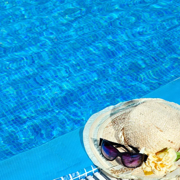 O chapéu de palha e os óculos de sol ficam perto da piscina — Fotografia de Stock