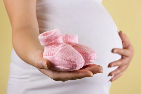 Femme enceinte tenant paire rose chaussures pour bébé fille — Photo
