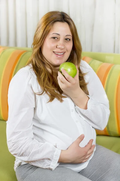 Happy pregnant woman eating a green apple — Stock Photo, Image