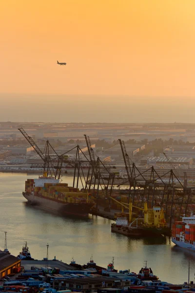 Vliegtuig en kranen op de haven van barcelona bij zonsondergang — Stockfoto