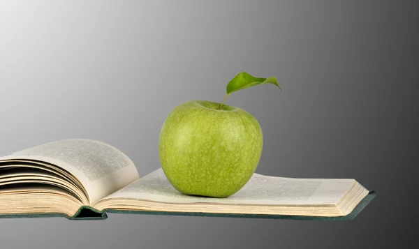 Зеленое яблоко на открытой книге — стоковое фото