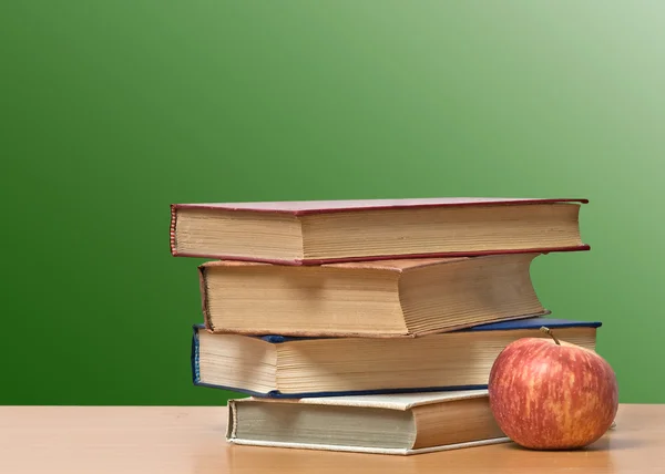 Rött äpple och böcker på skrivbord — Stockfoto