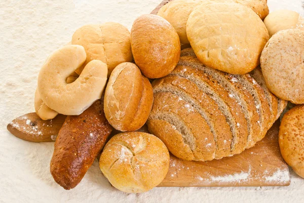 Various kinds of bread on the baking board sprinkled with flour — Stock Photo, Image