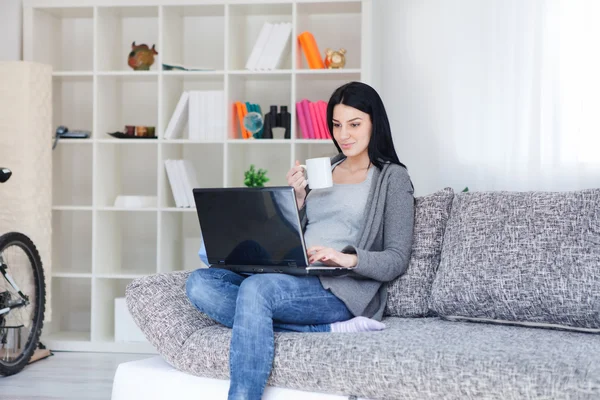 Kvinna med en mugg när du använder en bärbar dator — Stockfoto