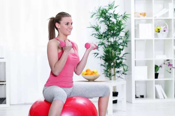 Mulher sentada em uma bola de fitness com halteres — Fotografia de Stock