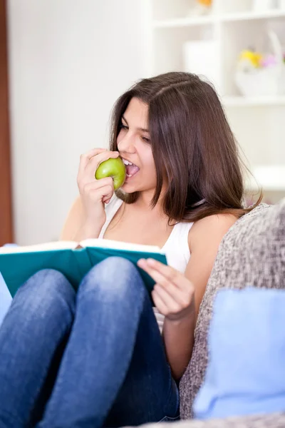 Yeme elma kanepede ve kitap okuma — Stok fotoğraf