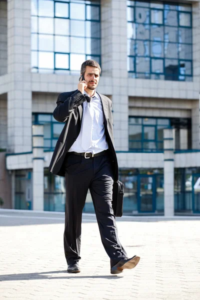 Businessman on the phone coming out of a building — Stock Photo, Image