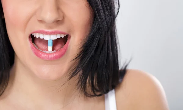 Women holding a pill in her teeth — Stock Photo, Image