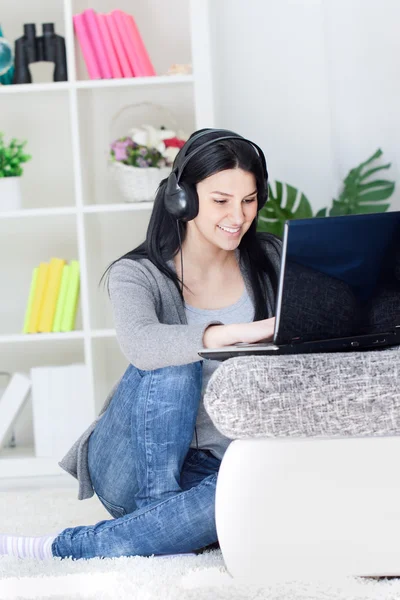Mujer bonita con ordenador y auriculares en casa — Foto de Stock